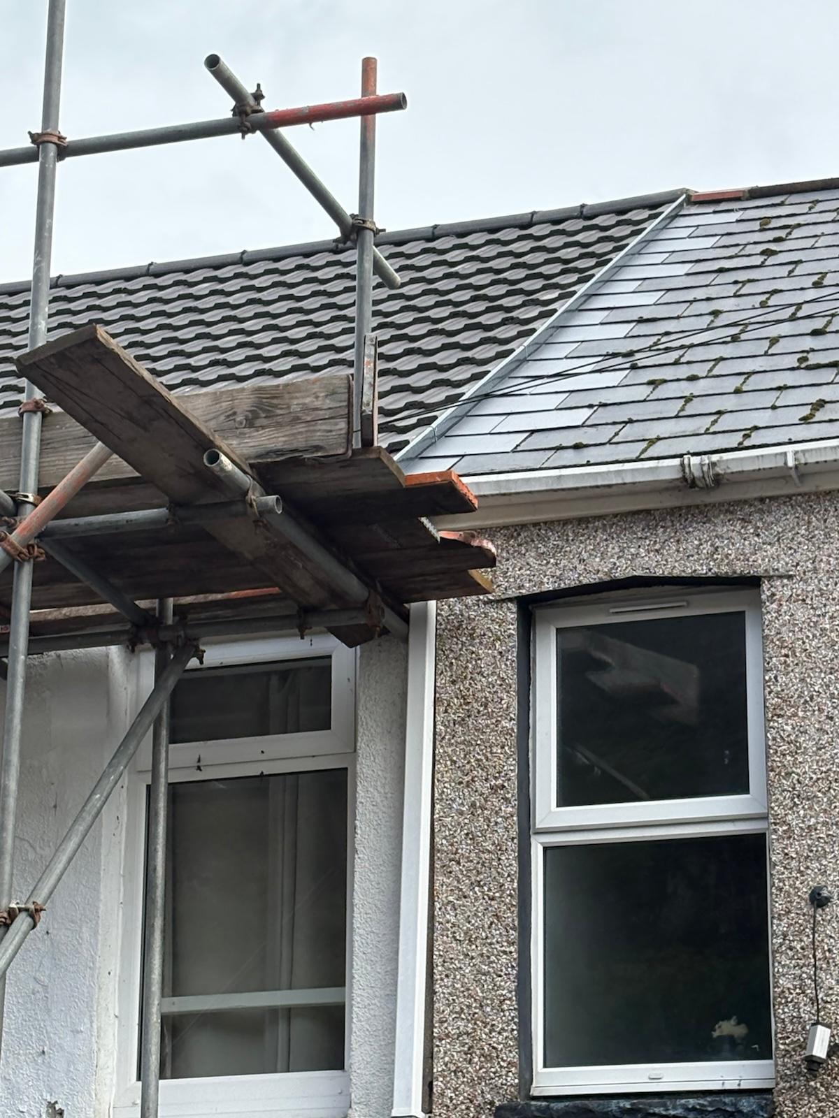New grey tiled roof meeting neighbouring slate with fresh lead flashing and new white fascia in Ebbw Vale